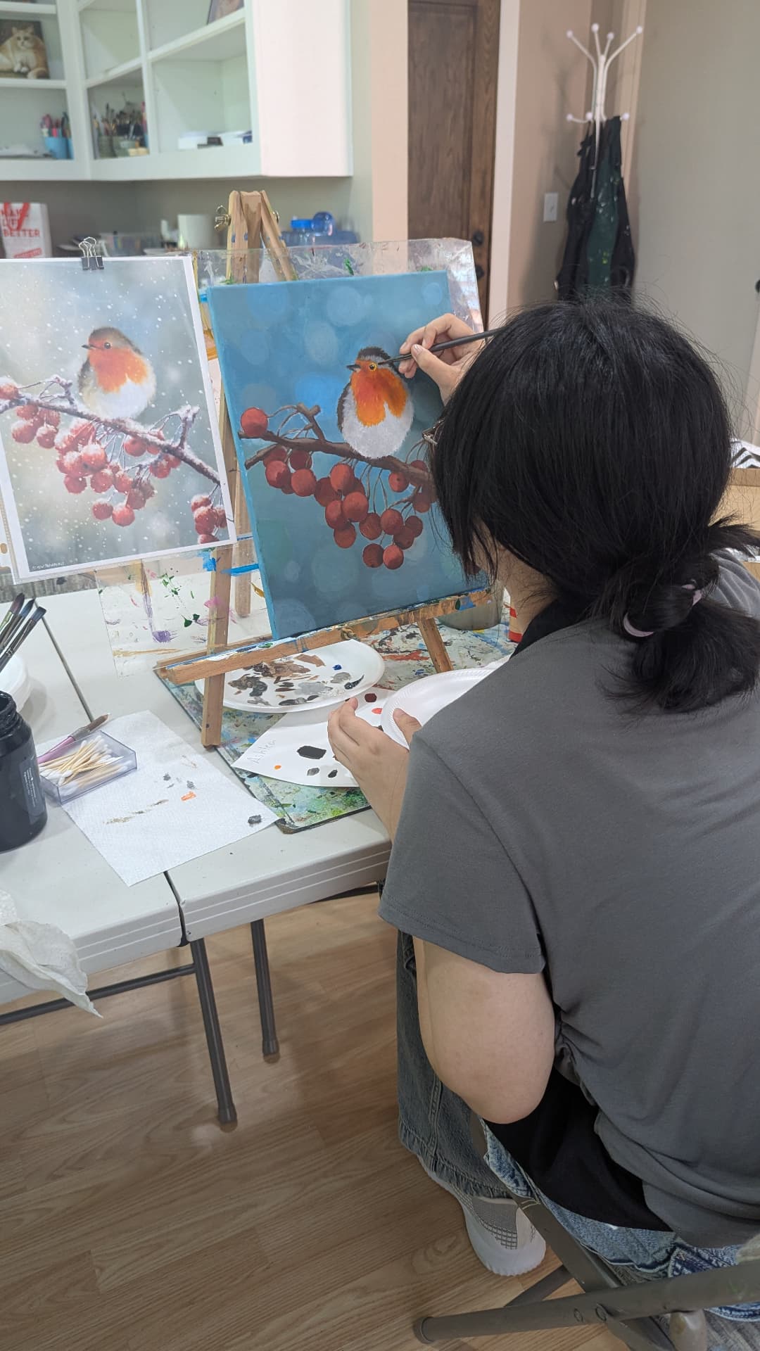 Adult student painting a robin on a berry branch in acrylic