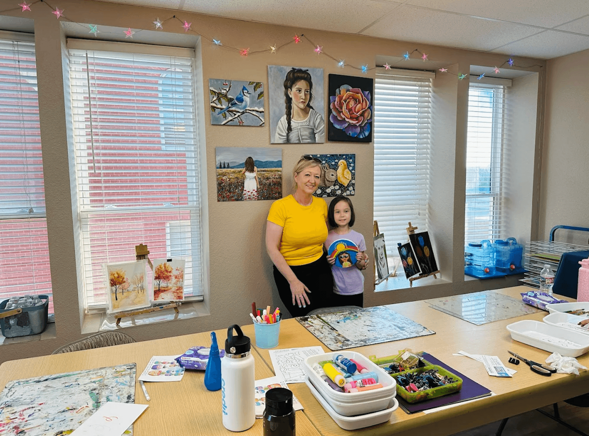 Iwona Staszewski with a young student inside the Art Adventure Studio classroom, surrounded by student paintings and art supplies